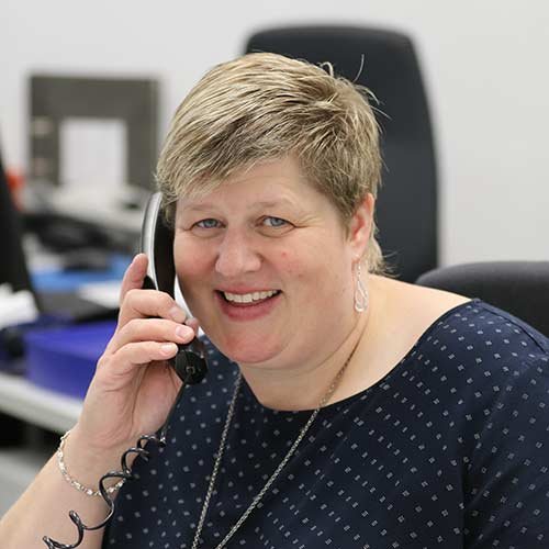 In einem hellen Büro lächelt eine Frau, die ein Telefon hält, und vermittelt eine positive, einladende Atmosphäre.