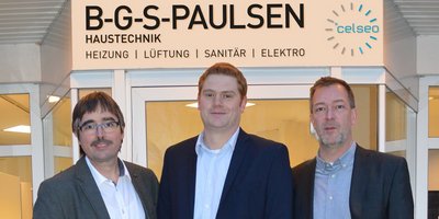 Drei Männer stehen vor einem modernen Gebäude mit einem Schild, das die Firma B-G-S-Paulsen für Haustechnik anzeigt.