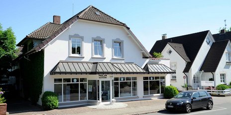 Ein helles, sonniges Bild eines Geschäftsgebäudes mit dem Namen 'Paulsen Haustechnik' über dem Eingang, umgeben von Bäumen.